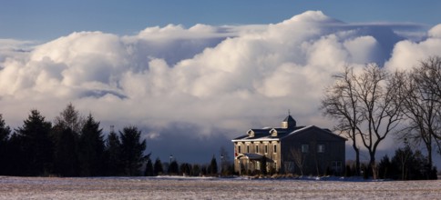 Color image of a house with large clouds in the background, set in a tranquil winter landscape in