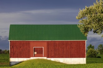 A red barn with a green roof against a cloudy sky in St. Thomas, Ontario, Canada, North America