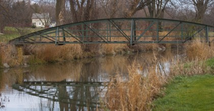 Rustic bridge over a creek with reflections, surrounded by autumn trees and grass, creating a
