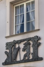 Window with blinds and metal relief, Gallus and the bear on the façade of the pharmacy in Kisslegg,