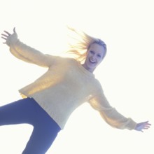 A smiling woman in casual clothes with a bright, light-filled background creating a joyful