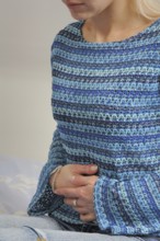 Young woman suffering, A woman in a blue striped sweater sitting indoors, clutching her hands over