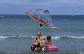 Family at the beach watching windsurfing. Two children with an adult, enjoying the sunny day