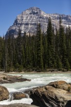 Majestic mountains behind a flowing river with rocky foreground inside Yoho National Park, in