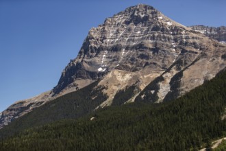 Dramatic mountain peak rising above a dense green forest as viewed from the Trans Canada Highway in