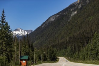 Open road curves through mountain pass with snow-capped peaks in the background in Revelstoke,