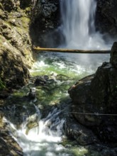 Cascading waterfall over rocks in sunlight in forest inside Cascade Falls Regional Park, Deroche,