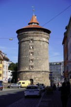 Massive round tower made of bricks, surrounded by city buildings under a clear sky, Nuremberg,