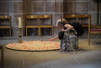 Woman lighting candles in a quiet church room, surrounded by chairs, St Lorenz Church, Nuremberg,