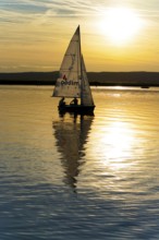 Lake Neusiedl, Burgenland, Austria, Europe, Single sailboat at sunset with reflecting light on calm