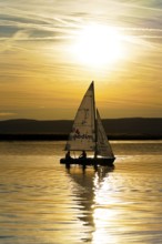 Lake Neusiedl, Burgenland, Austria, Europe, Sailboat at sunset with reflection on calm water under