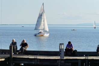 Lake Neusiedl, Burgenland, Austria, Europe, People sitting at the jetty and watching a sailing boat