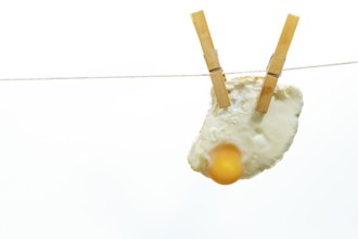 Clothespins holding fried egg on clothesline against white background, creating a quirky and