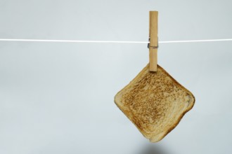Toasted bread hanging on clothesline with clothespin against white background