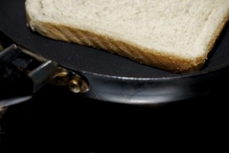 Close-up of a single slice of white bread toasting in a frying pan, suggesting a simple breakfast