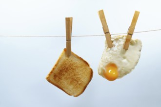 Toasted bread and fried egg are hanging from a clothesline with wooden clothespins, representing a