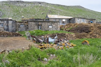 Stone house in a rural area surrounded by green hills and rocks, cow dung in front, Ardenis, Shirak