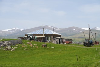 A farm with tractors and a stone house in front of a mountain landscape, Zorakert, Lake Arpi,