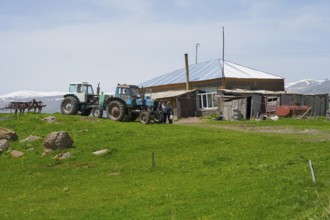Two tractors standing on a green field next to a farmhouse and a barn, Zorakert, Lake Arpi, Shirak