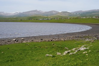 Tranquil lake with a view of green hills and distant mountains on the horizon, Lake Arpi, Shirak