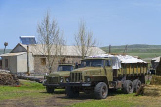 Large lorries parked on a farm in front of a stone building surrounded by green countryside, Gaz 53