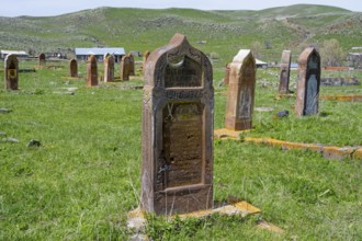 A well-preserved old gravestone on green grass in front of a hilly landscape with several