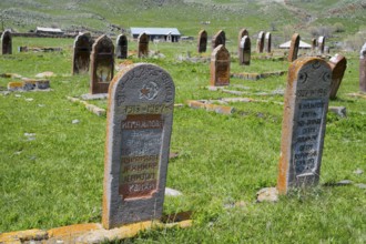 Close-up of two gravestones in a grassy cemetery with rolling hills in the background, old