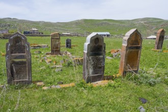 Cemetery with old weathered gravestones on green grassland with rolling hills in the background,