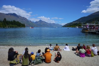 Groups of people sitting on the beach enjoying the view of the lake and mountains, Queenstown,