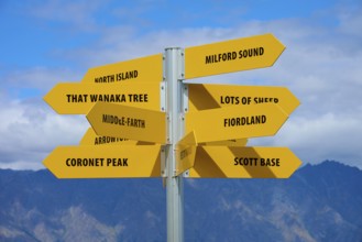 Yellow signpost with several signs and a mountain ridge in the background against a blue sky,