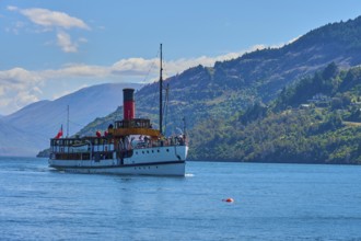 Large ship sailing across a wide lake with picturesque mountain ranges in the background,
