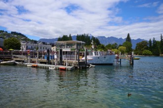 Harbour with boats and buildings on calm lake under partly cloudy sky, Queenstown, Queenstown-Lakes