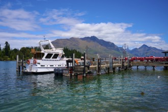 Boat at a jetty on a tranquil lake with surrounding mountain scenery, Queenstown, Queenstown-Lakes