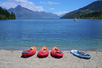 Red kayaks and paddleboard on the beach in front of a calm lake with mountain views, Queenstown,