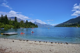 Waters with floating ducks and boats against a picturesque mountain backdrop and clear skies,