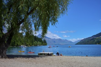 Sunny day at the lake with calm water, people relaxing on the shore and boats floating on the