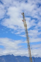 High crane rises into a blue sky with white clouds, mountain landscape in the background,