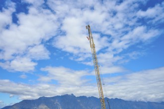 A tall construction crane erected against a cloudy sky with a mountain backdrop, Queenstown,