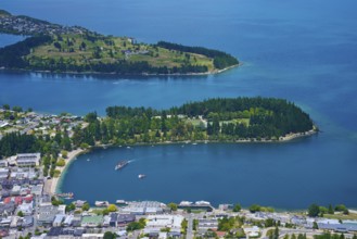 Aerial view of an urban landscape with a blue-green lake and forested peninsulas, Queenstown,