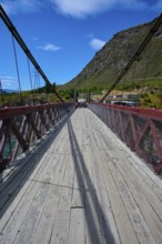 Wooden footbridge with red railing, shadows and mountain background, Kawarau Gorge Suspension