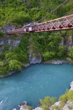 Red suspension bridge over river with steep wooded cliffs and calm waters, Kawarau Gorge Suspension