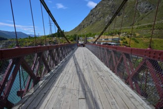 Wooden footbridge with cables and mountain backdrop on a clear, sunny day, Kawarau Gorge Suspension