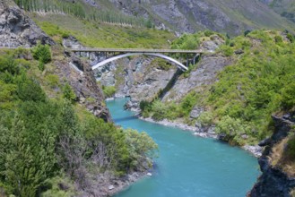 A bridge spans a turquoise-coloured river in a green and rocky landscape, Kawarau River,