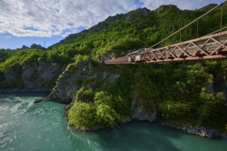 Red suspension bridge with view over the turquoise river and green surroundings, Kawarau Gorge