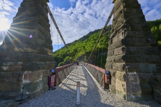 Old bridge with massive stone pillars surrounded by lush greenery under a bright blue sky, Kawarau