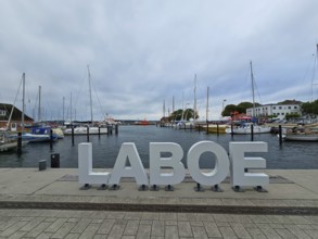 LABOE lettering at the edge of the harbour, surrounded by sailing boats and a cloudy sky, Laboe,