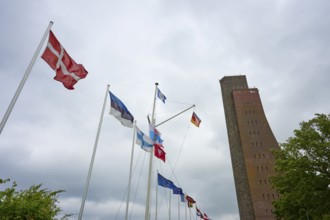 National flags next to a high brick tower under a cloudy sky, Naval Memorial, Laboe, Kiel Fjord,