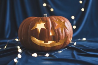 Carved Halloween pumpkin with star eyes glowing on black fabric with festive lights. Generative AI,