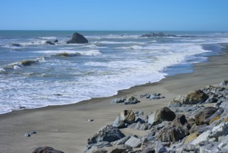 The waves gently lap against a wide sandy beach with scattered rocks, West Coast, South Island, New