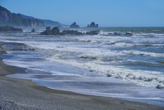 Dynamic waves roll onto a rocky beach under a bright blue sky, West Coast, South Island, New